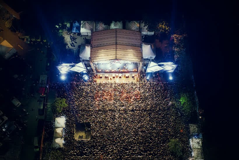 Vista aérea de um público reunido diante de um palco iluminado à noite