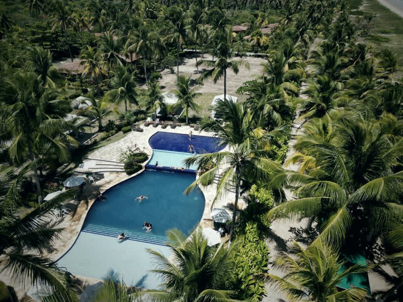 Vista aérea de um resort com piscinas cercadas por coqueiros